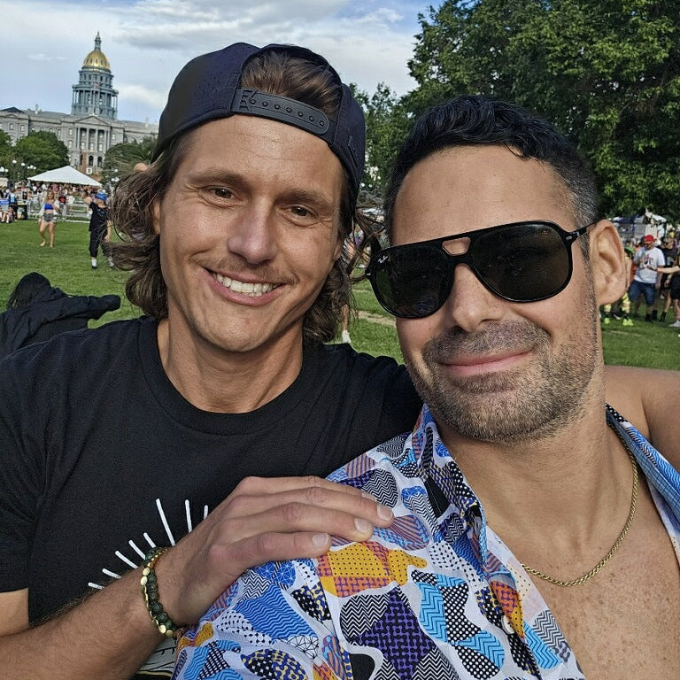Two handsome men taking a selfie outdoors with a building and trees in the background